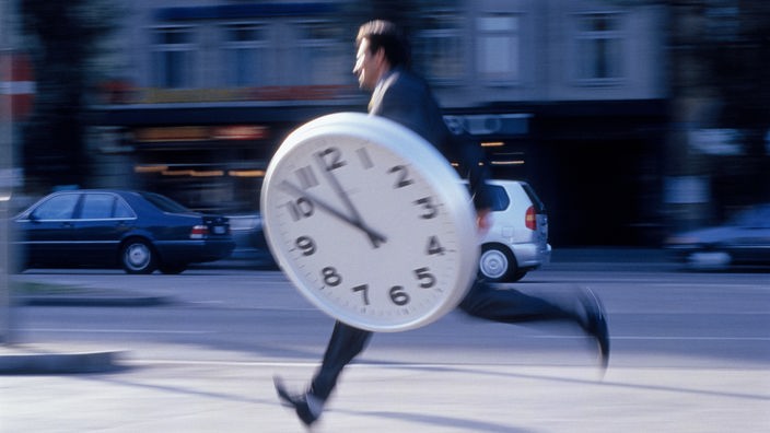 Symbolfoto: Silhouette eines rennenden Menschen mit einer großen Uhr in der Hand