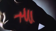 Silhouette einer Frau, die sich an die linke Brust fasst. Im Bereich des Herzens ist graphisch eine rote Zickzacklinie (Herzschlag) zu erkennen.