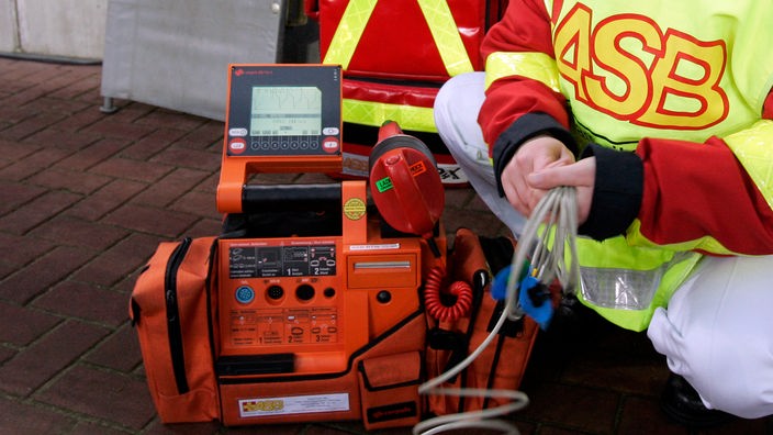 Ein Mitarbeiter des 'ASB' kniet neben einem orangefarbenen elektronischen Gerät.