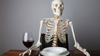 Menschliches Skelett sitzt mit einem Glas Wein am Tisch