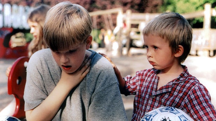 Ein kleiner Junge legt seinem nach Luft ringenden Spielkameraden eine Hand auf die Schulter