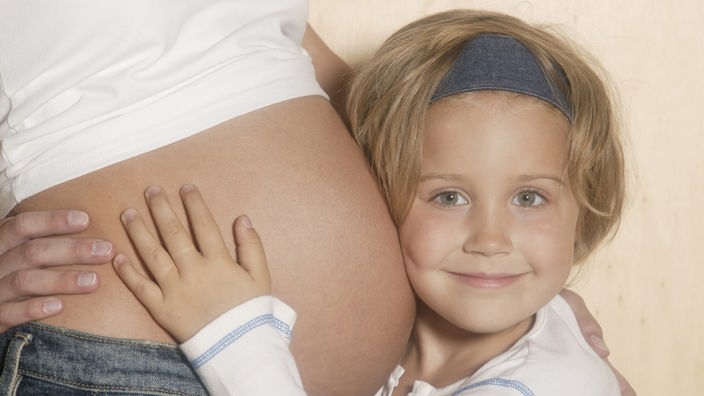 Mädchen streichelt den schwangeren Bauch seiner Mutter.