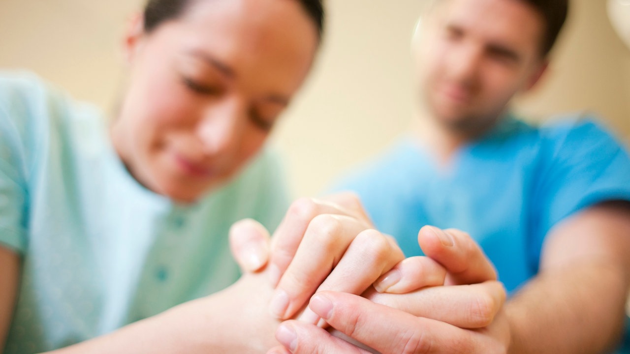 Hebamme und Mann halten Hand von einer Schwangeren.