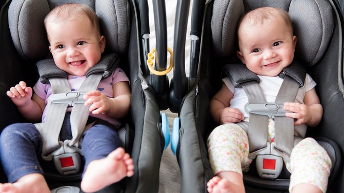 Zwillingsbabys nebeneinander in zwei Autositzen