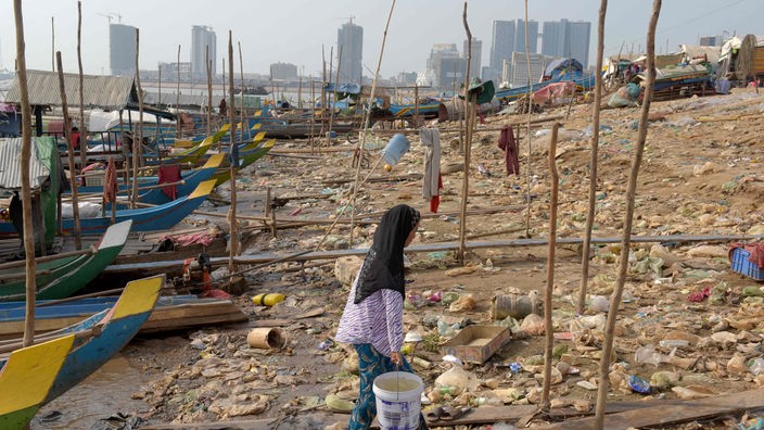 Boote und Müll am Ufer des Mekong, im Hintergrund Hochhäuser