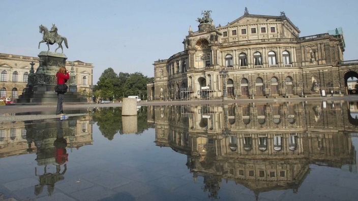 Der Platz vor der Dresdener Semperoper ist überflutet. Das Gebäude spiegelt sich im Wasser. Eine Frau fotografiert die Szene.