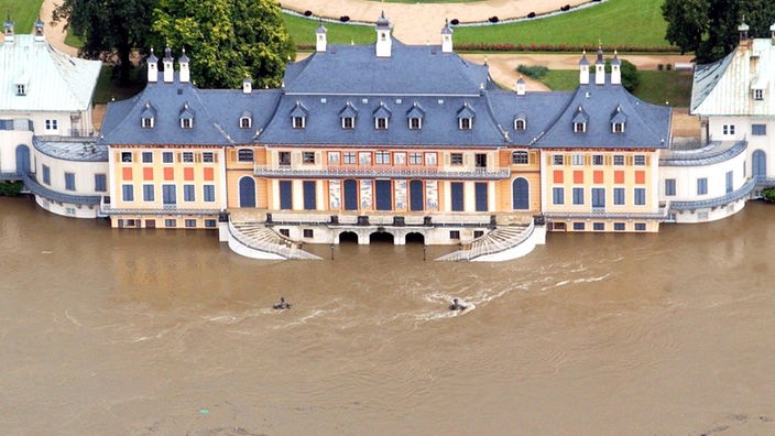 Luftbild: Schloss Pillnitz, ein herrschaftliches großes Gebäude mit geschwungener Freitreppe, steht mit der Vorderseite im Wasser.