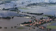 Luftbild: Die weit über die Ufer getretene Elbe ähnelt eher einem See als einem Fluss. Vereinzelt schauen Bäume aus dem Wasserteppich. Am Rand des Wassers ist ein Dorf zu sehen