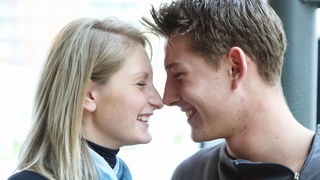 Ein Paar gibt sich mit verliebtem Lächeln einen Nasen-Kuss.