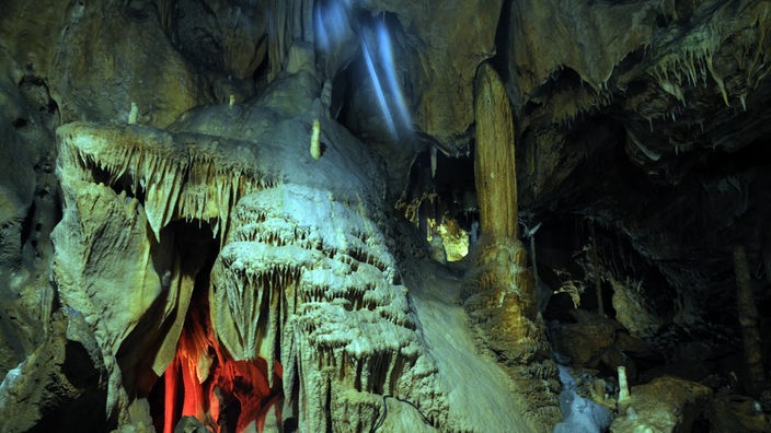 Mehrere Tropfsteinsäulen werden in einer Höhle angeleuchtet
