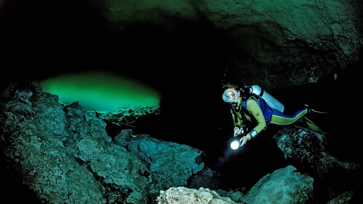 Höhlentaucherin mit eingeschalteter Taschenlampen zwischen den Felswänden eines weiten Höhlenganges