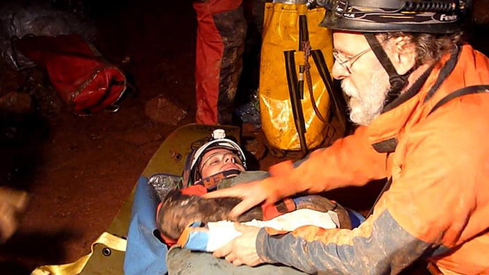 Bei einer Höhlenrettungsübung liegt ein Verletzter auf einer Rettungsliege; ein Helfer kniet neben ihm