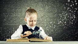 Ein Mädchen sitzt mit einer Lupe über einem aufgeschlagenen Buch, dahinter eine Tafel voller Mathematikformeln