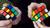 Zwei Hände drehen an zwei Rubik-Würfeln