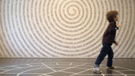 Fotografie eines Kindes vor einer Wand, auf der die Stellen der Zahl Pi spiralförmig angeordnet sind