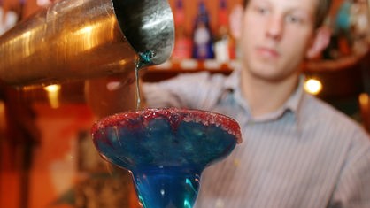 Barkeeper schüttet Flüssigkeit aus einem Cocktailshaker in ein Glas.