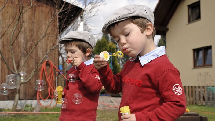 Zwei eineiige Zwillingsjungen im Alter von vier Jahren pusten Seifenblasen.