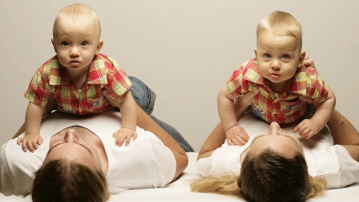 Mutter und Vater liegen auf dem Rücken, beide haben jeweils einen Zwillingsjungen auf dem Bauch.
