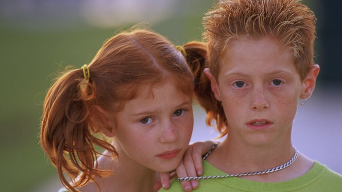 Ein Mädchen und ein Junge mit roten Haaren und grünem Oberteil stehen beieinander
