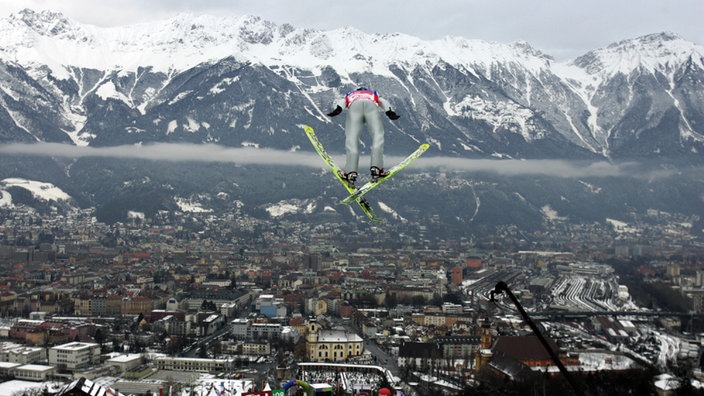 Ein Skispringer fliegt bei der Vierschanzentournee von der Bergiselschanze scheinbar über dem österreichischen Innsbruck mit seinen schneebedeckten Bergen im Hintergund. | Bildquelle: dpa/Matthias Schrader Ein Skispringer fliegt bei der Vierschanzentournee von der Bergiselschanze scheinbar über dem österreichischen Innsbruck mit seinen schneebedeckten Bergen im Hintergund.