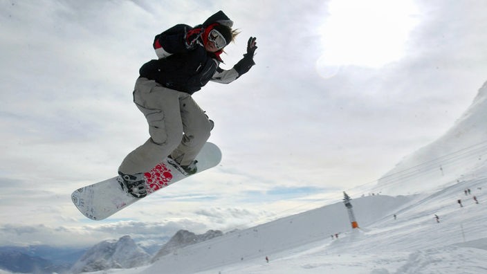 Ein Snowboarder liegt auf einer Piste quer in der Luft.