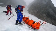 Männer der Bergwacht mit Rettungsschlitten im Schnee vor Berg