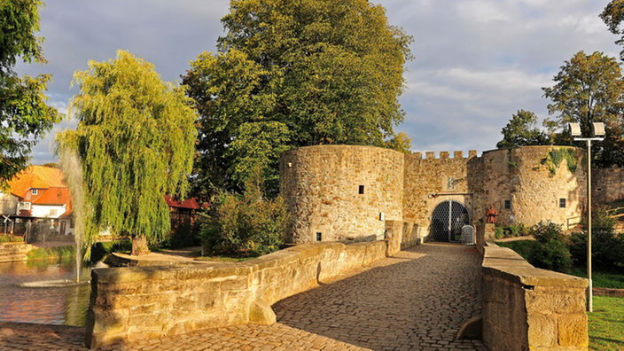 Eine mittelalterliche Burg. Der Zugang führt über einen Wassergraben. Links und rechts des Toreingangs befinden sich Rundtürme.