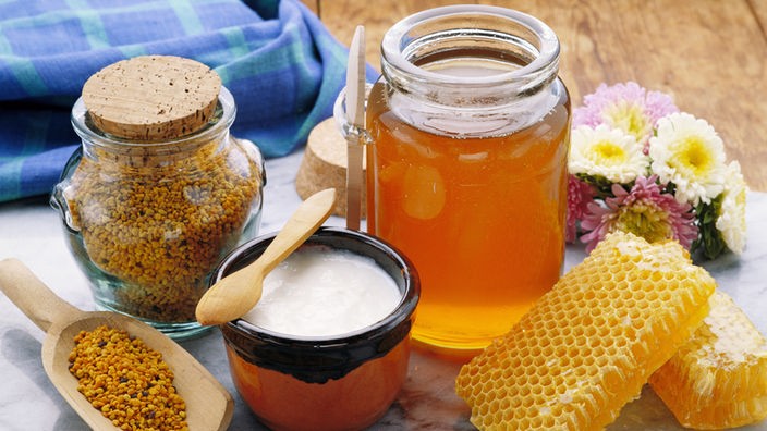 Auf einem Marmorbrett stehen verschiedene Bienenprodukte, wie Honig, Propolis, Gelee Royal und gefüllte Honigwaben.