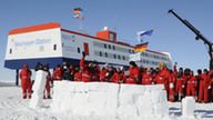Eine Polarstation im Eis, davor Menschen in roten Anzügen.