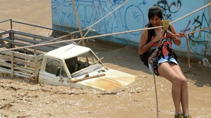 Eine junge Frau wird mit einer Seilwinde über eine überflutete Straße transportiert