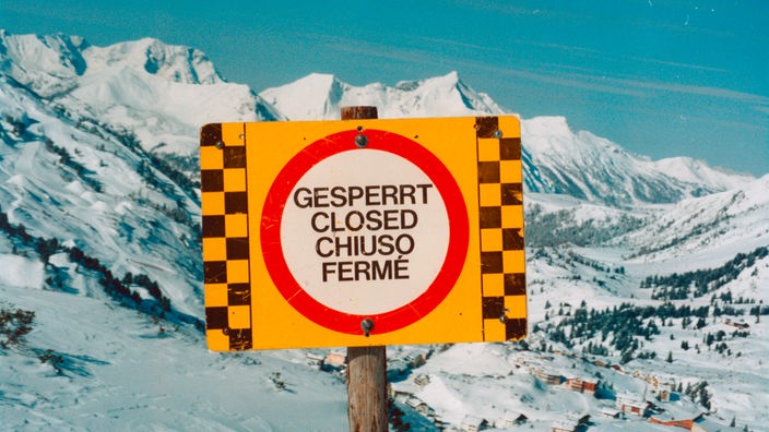 Schild vor Alpenlandschaft, auf dem in verschiedenen Sprachen "Gesperrt" steht