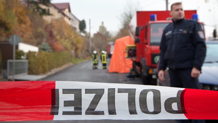 Polizeiabsperrband, dahinter Einsatzkräfte auf einer Straße in Schmalkalden | Bildquelle: dpa/Michael Reichel Polizeiabsperrband, dahinter Einsatzkräfte auf einer Straße in Schmalkalden