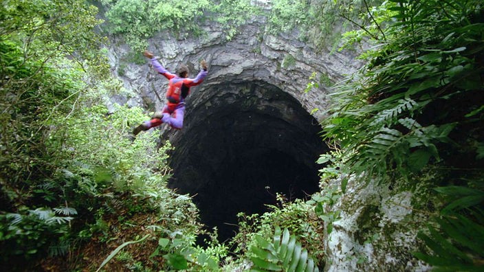 Fallschirmspringer fällt in großes schwarzes Loch im Gestein