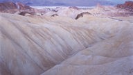 Elfenbeinfarbene Felsen am Zabriskie Point im Nationalpark Death Valley in Kalifornien, im Hintergrund ist ein breites Tal zu erkennen.