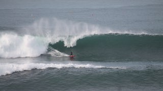 Tony Butt surft eine riesige Welle auf einem roten Surfbrett