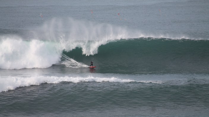 Tony Butt surft eine riesige Welle auf einem roten Surfbrett