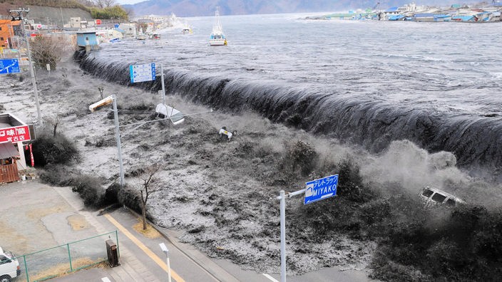 Auftreten der Riesenwelle an der Küste von Miyako, Japan. Autos und LKWs verschwinden in den Fluten.