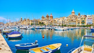 Mehrere Fischerboote und Yachten in einem Hafen vor einer maltesischen Stadt.