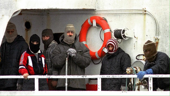 Männer mit Mützen stehen auf einem Schiffsdeck