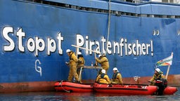 Greenpeace-Schlauchboot neben Schiff eines Piratenfischers. Die Aktivisten pinseln den Schriftzug "Stoppt Piratenfischer" auf das andere Schiff