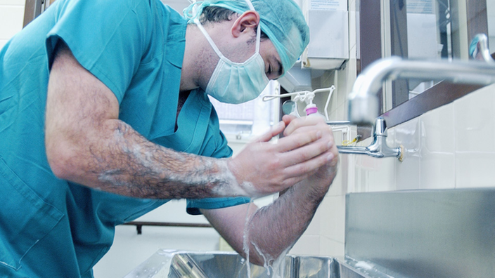 Ein Arzt in OP-Kleidung wäscht und desinfiziert sich die Hände.