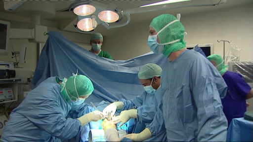 Mehrere Ärzte in Schutzkleidung bei einer Operation im OP-Saal.