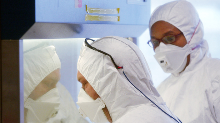 Zwei Forscher in weißen Anzügen und mit Mundschutz in einem Labor.