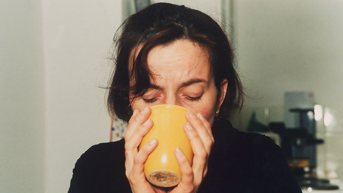 Eine Frau hält eine Tasse Tee in beiden Händen und trinkt daraus.