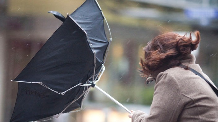 Eine Frau versucht bei Sturm ihren Schirm festzuhalten