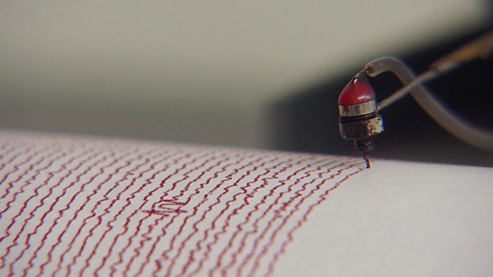 Erdbebenschreiber malt rote Wackellinien auf weißes Papier.