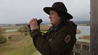 Eine Rangerin vom Nationalpark Unteres Odertal beobachtet Singschwäne auf den überfluteten Auenwiesen