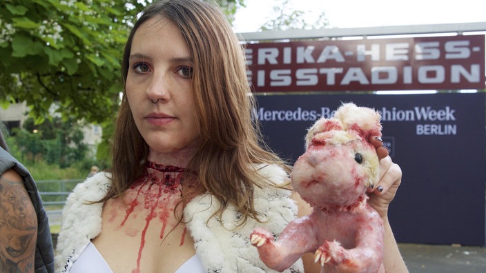 Das Bild zeigt eine Frau mit einer Kunstblutwunde am Hals. In der linken Hand hält sie eine Nachbildung eines Kaninchens, dessen Fell abgezogen wurde. | Bildquelle: imago/epd/Rolf Zoellner Das Bild zeigt eine Frau mit einer Kunstblutwunde am Hals. In der linken Hand hält sie eine Nachbildung eines Kaninchens, dessen Fell abgezogen wurde.