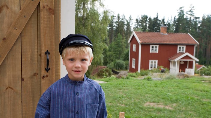 Verkleideter Junge als Michel vor einem roten Holzhaus.