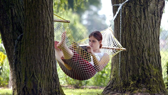 Eine Frau liegt in einer Hängematte, die zwischen zwei Bäumen gespannt ist.